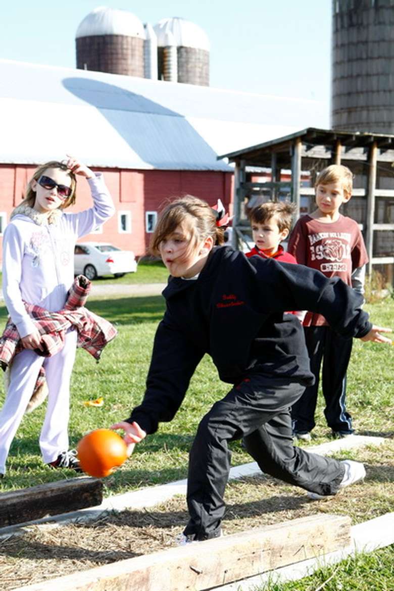 one child bowling with a pumpkin while other kids look on